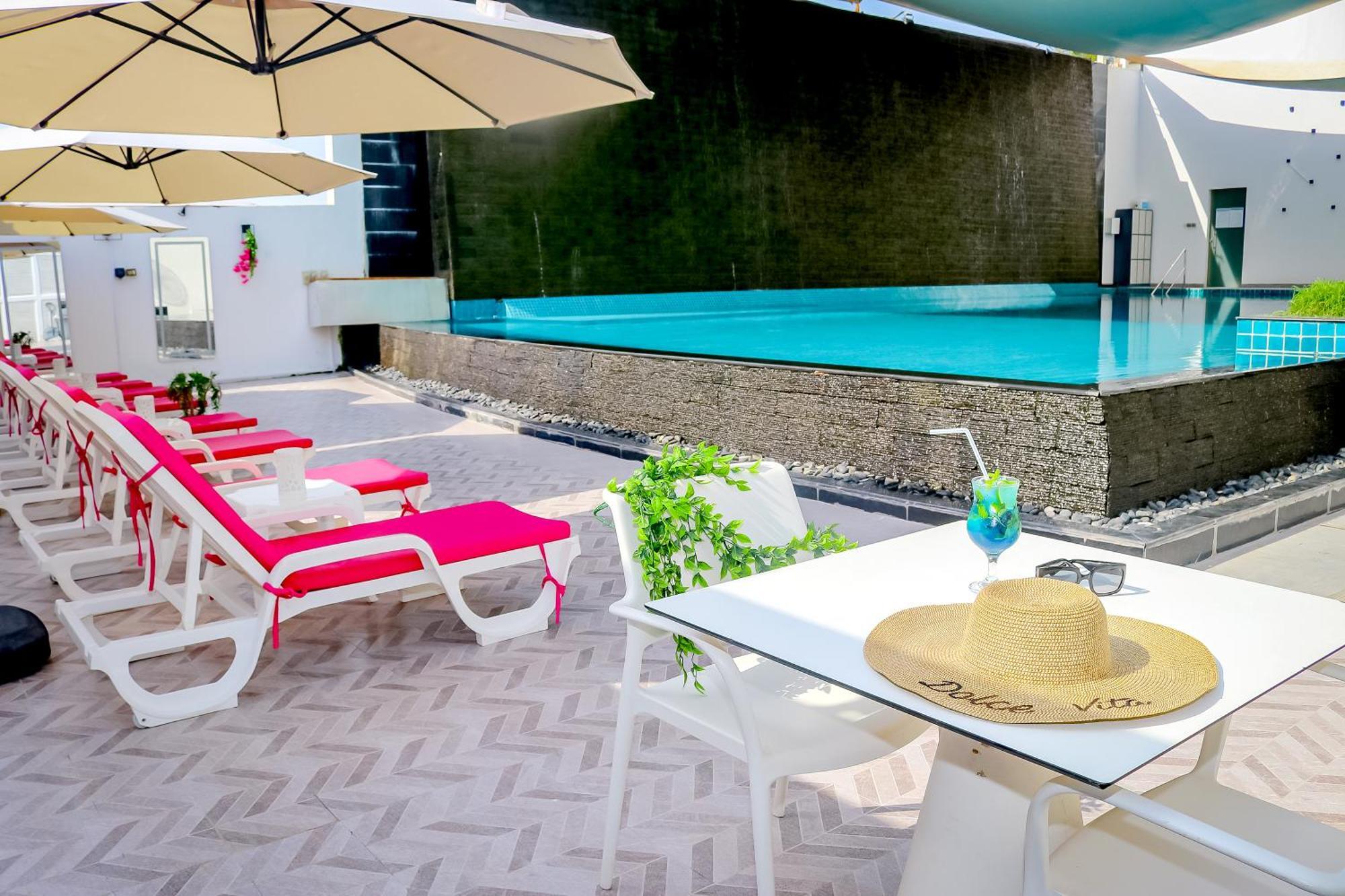 Lagoona Beach Luxury Resort And Spa Manama Exterior foto The photo shows a sunny poolside area with bright red lounge chairs arranged neatly beside a swimming pool. There are large beige umbrellas providing shade. A small table is set up with a straw hat and a colorful drink, suggesting a relaxed, tropical