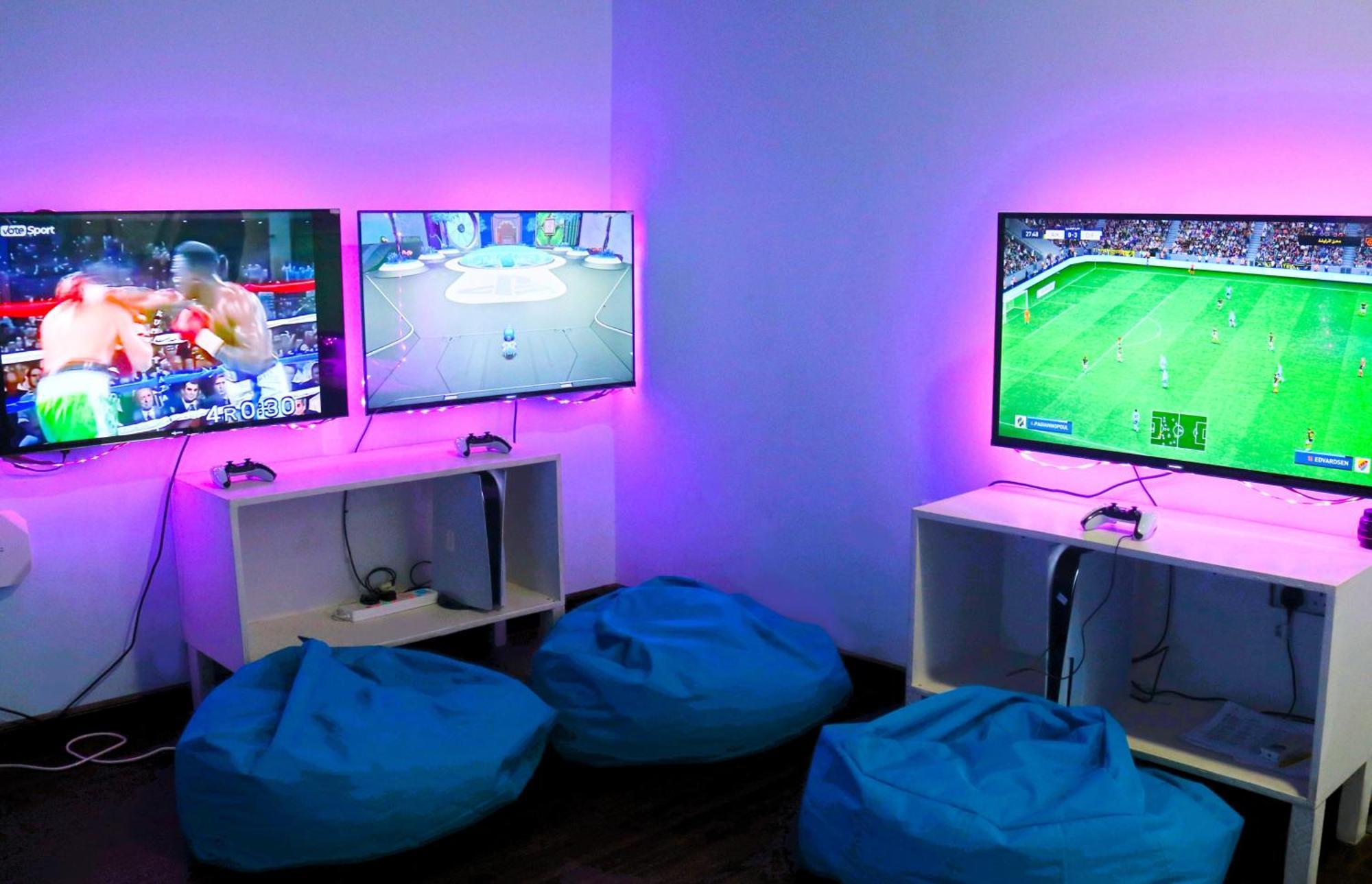 Lagoona Beach Luxury Resort And Spa Manama Exterior foto The photo shows a gaming area featuring three televisions mounted on the wall, displaying different games. Two of the TVs are showing gaming scenes, with one depicting a boxing game and the other showing a vibrant game environment. The third TV displ