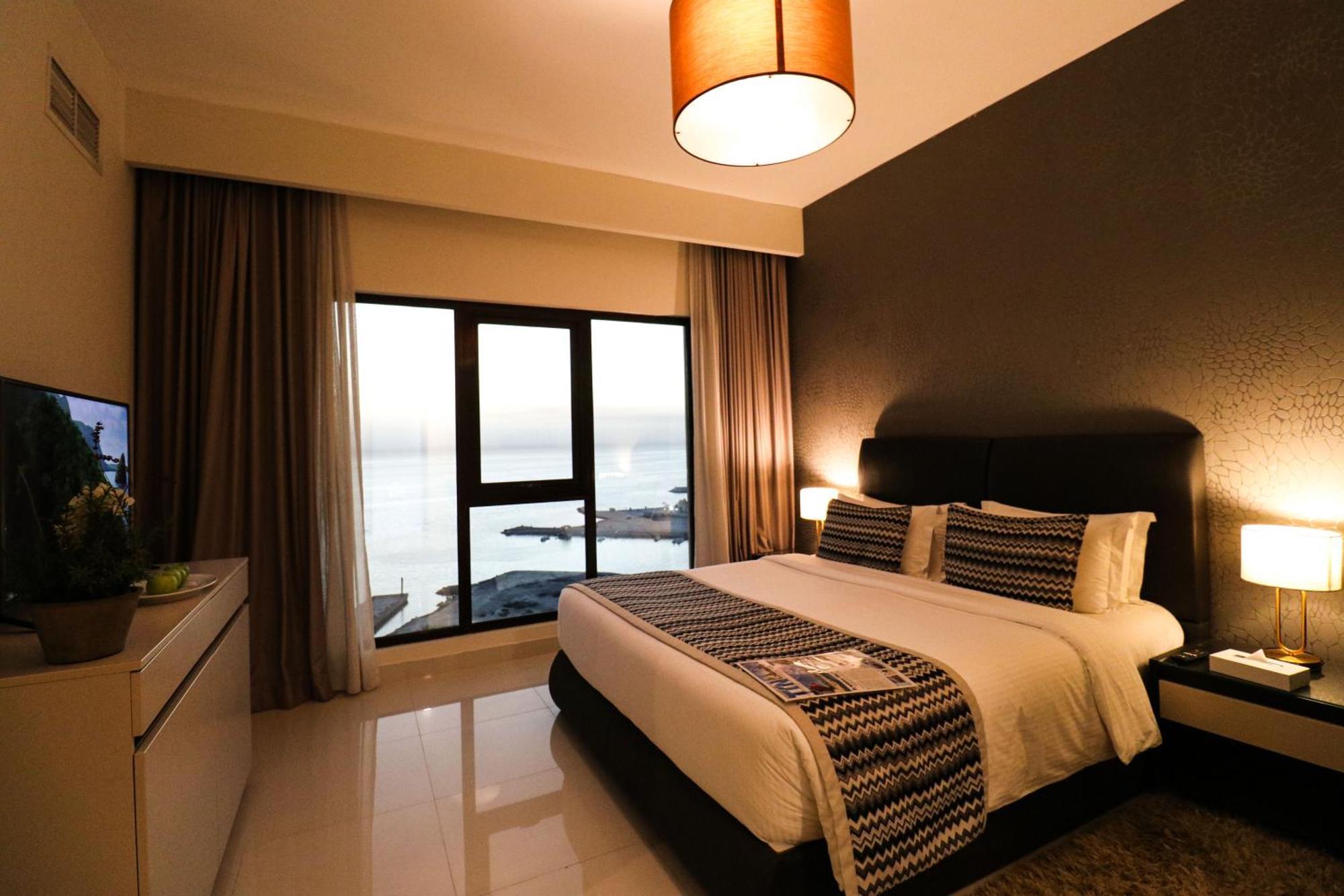 Lagoona Beach Luxury Resort And Spa Manama Exterior foto The photo shows a modern hotel room featuring a neatly made bed with decorative pillows. The room has a stylish design with a dark accent wall and a large window that offers a view of the outdoors. Natural light comes in, giving the space a bright an