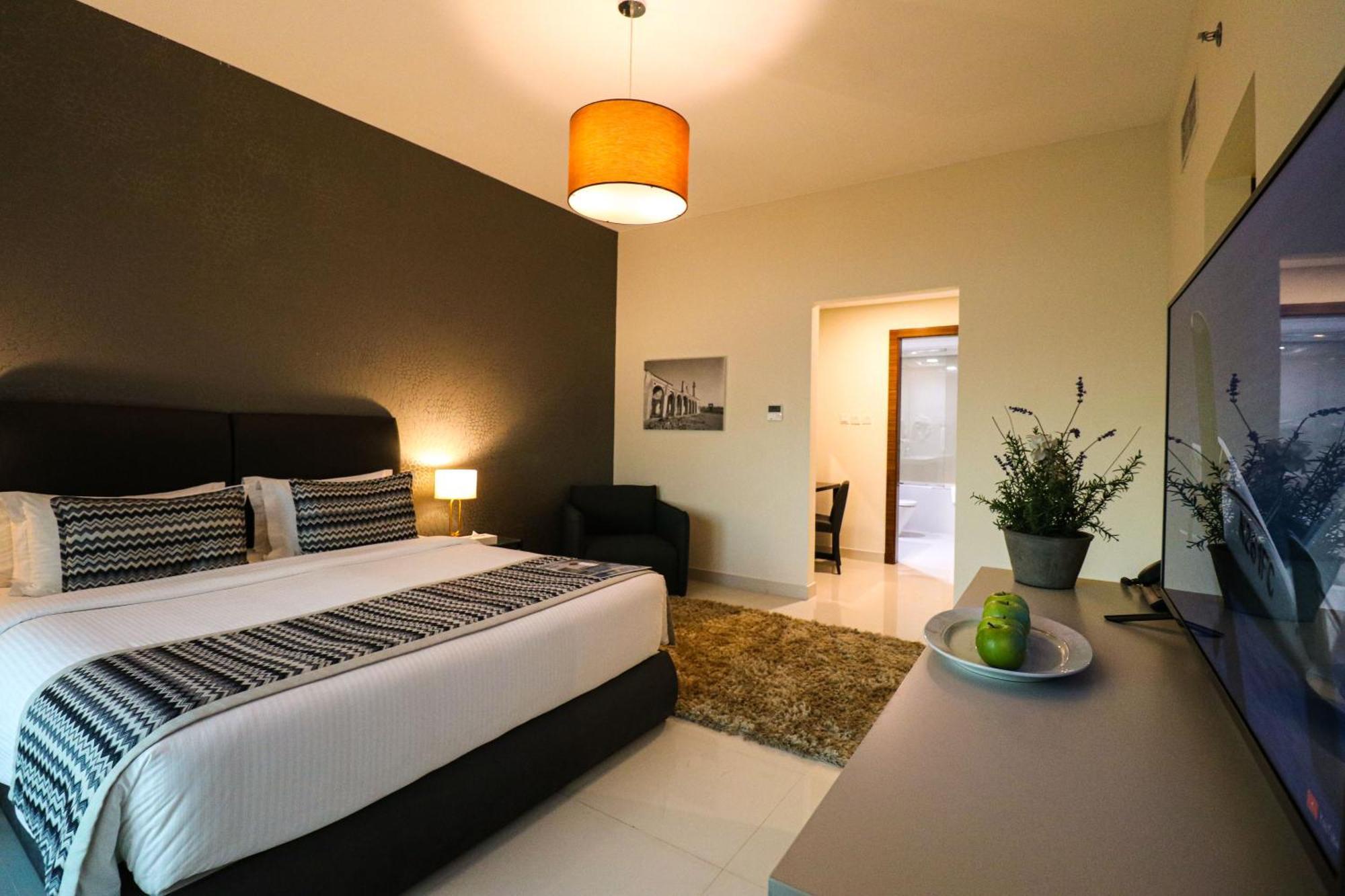 Lagoona Beach Luxury Resort And Spa Manama Exterior foto The photo shows a modern hotel room. It features a large bed with a neatly made white and dark-colored duvet. On either side of the bed, there are bedside tables with lamps. The wall behind the bed is painted in a dark color, creating a contrast with